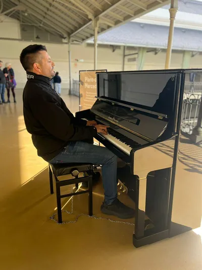 Marios Tsopouridis playing an upright piano in a sunlit hall